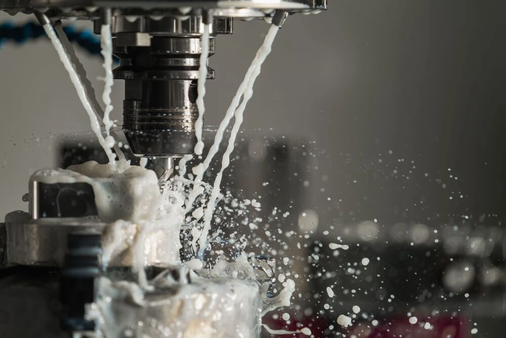 CNC milling machine cutting a metal workpiece with coolant spraying during precision machining.